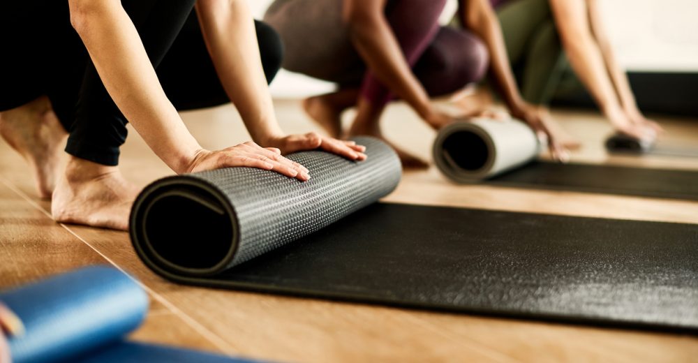 Close-up of athletic women preparing their exercise mats for sports training at health club. Focus is on woman in black.